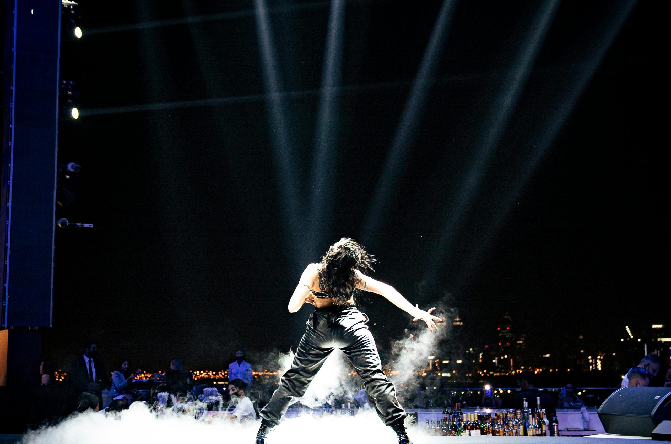 A powerful back view of a performer on stage with dramatic city skyline at night.